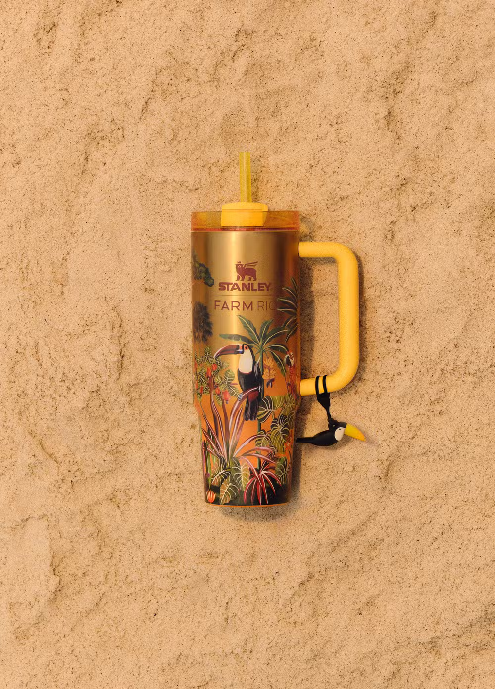 Copo térmico Stanley x FARM Rio com estampa tropical e tampa, com canudo amarelo, sobre fundo de parede bege