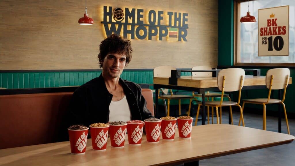 Fiuk em uma lanchonete do Burger King, ao lado de BK Shakes em copos, com banner “Home of the Whopper”.
