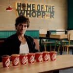 Fiuk em uma lanchonete do Burger King, ao lado de BK Shakes em copos, com banner “Home of the Whopper”.