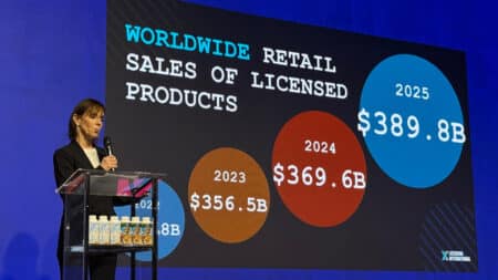 Gráfico de vendas de produtos licenciados em evento de licenciamento Palestrante em evento com gráfico de vendas de produtos licenciados no telão: 2023, 2024 e 2025.