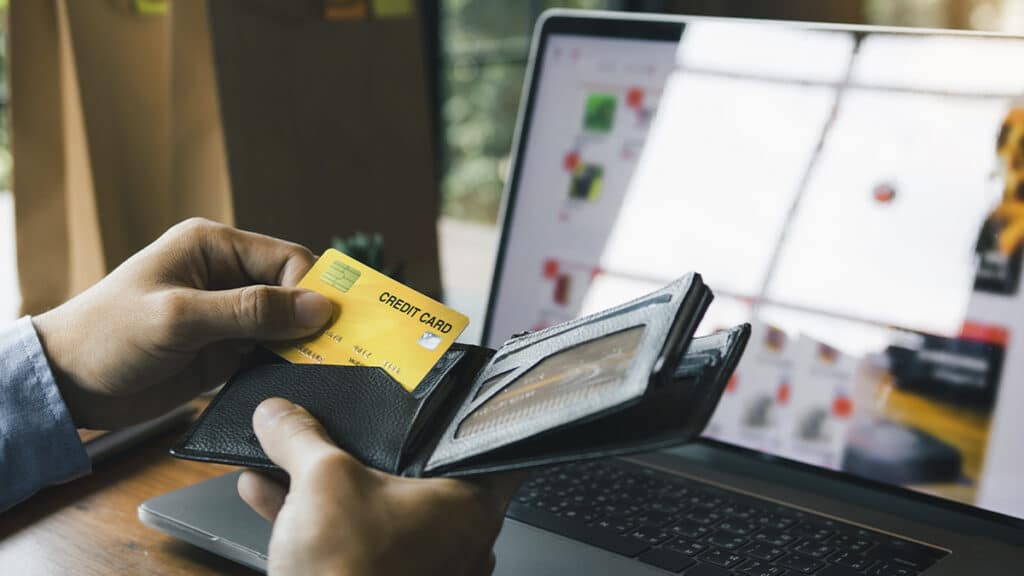 Geração Z e golpes digitais: pagamento com cartão e notebook Pessoa paga com cartão de crédito enquanto usa notebook, cenário de golpes digitais e perdas financeiras da Geração Z