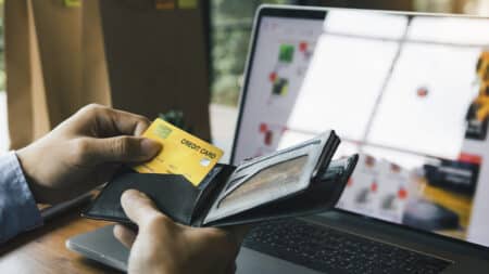 Geração Z e golpes digitais: pagamento com cartão e notebook Pessoa paga com cartão de crédito enquanto usa notebook, cenário de golpes digitais e perdas financeiras da Geração Z