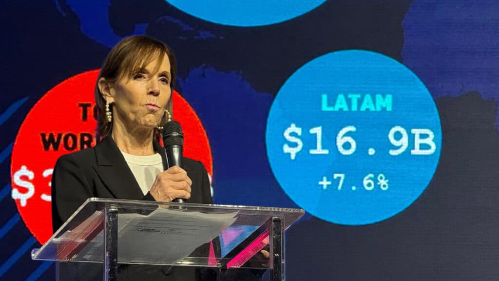 Palestrante em evento com telão mostrando LATAM US$ 16.9B e +7.6% ao lado do cenário