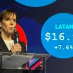 Palestrante em evento com telão mostrando LATAM US$ 16.9B e +7.6% ao lado do cenário
