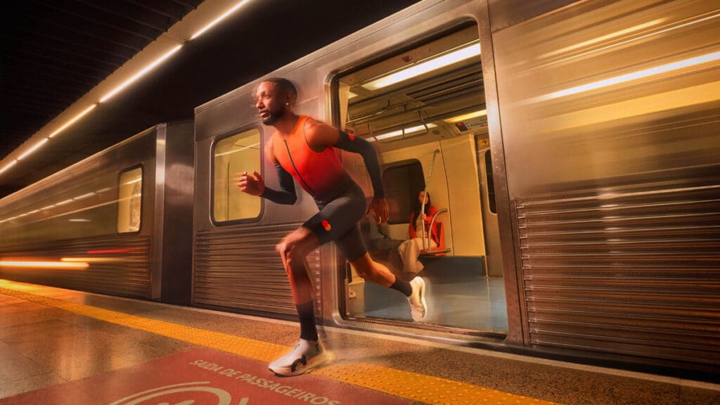 Velocista em corrida dentro de um metrô, ao lado da porta aberta, com iluminação noturna e movimento no túnel.