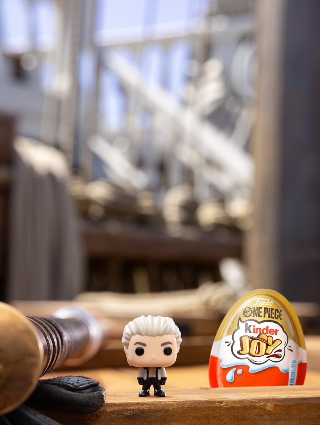 Miniatura colecionável de One Piece ao lado de ovo Kinder Joy em mesa, com embalagem ao fundo