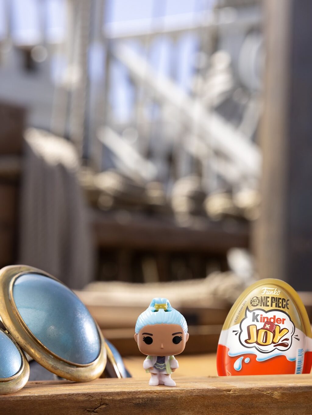 Boneco colecionável de One Piece com embalagem da Kinder Joy, em mesa com fundo desfocado.