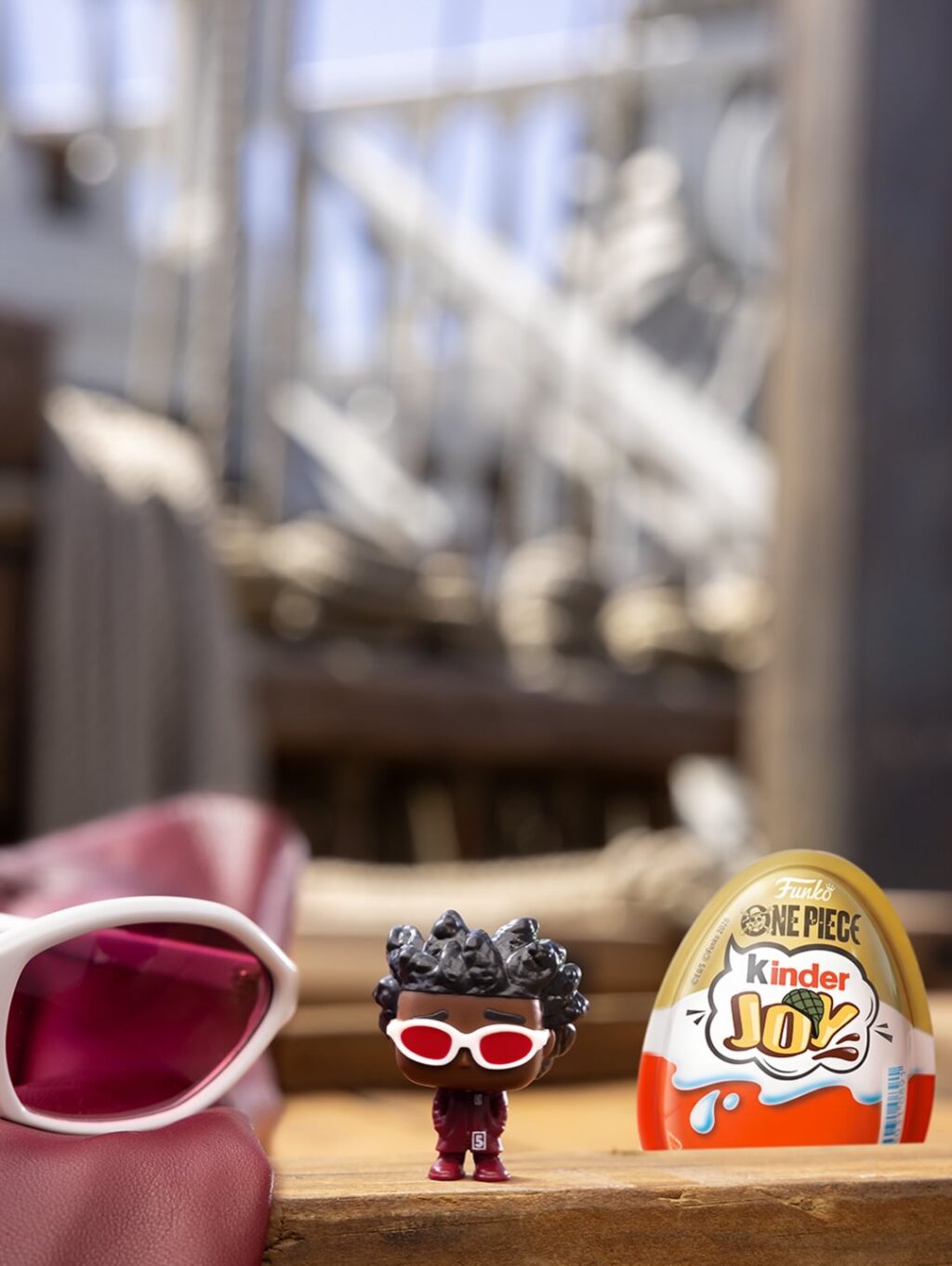 Colecionável de One Piece com mini figura usando óculos em miniatura ao lado de Kinder Joy, com embalagem One Piece.