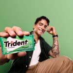 Maluma em campanha da Trident, segurando embalagem verde de goma de mascar em fundo verde