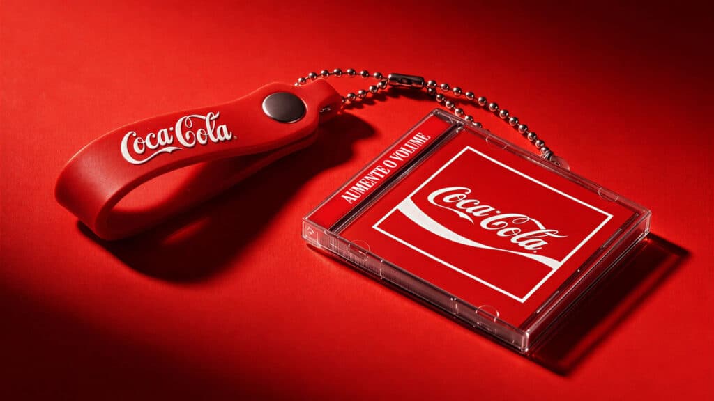 Mini CD-brinde Coca-Cola para o Rock in Rio 2026 Mini CD-brinde da Coca-Cola sobre fundo vermelho, com chaveiro em formato de mini CD