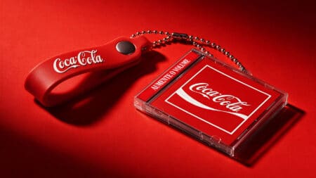 Mini CD-brinde Coca-Cola para o Rock in Rio 2026 Mini CD-brinde da Coca-Cola sobre fundo vermelho, com chaveiro em formato de mini CD