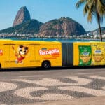 Ônibus amarelo da Paçoquita com personagens e adesivo do produto em frente ao Pão de Açúcar, no Rio de Janeiro.