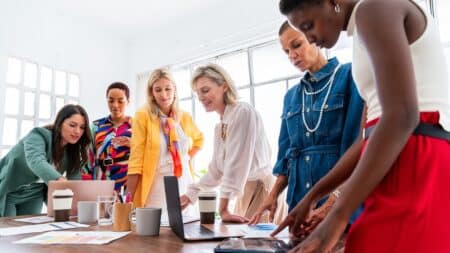 Pesquisa Pride Content: mulheres na agência e desigualdade salarial Equipe de mulheres em agência de publicidade analisando documentos e usando computador em reunião