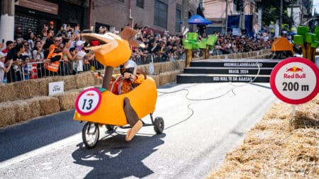 Participantes no Red Bull Ladeira Abaixo, descida com público Participantes em uma corrida de carrinhos descendo uma ladeira, com placas Red Bull e público nas laterais
