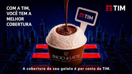 TIM e Bacio di Latte: cobertura de gelato Pote de sorvete Bacio di Latte com calda e ícones da TIM, em fundo de cidade à noite e frase sobre cobertura