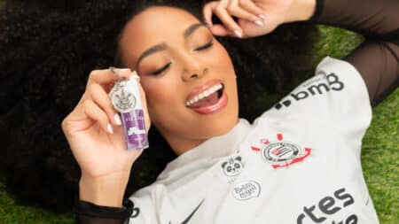 Vizzela e Corinthians: batom em parceria com as Brabas Mulher sorrindo com batom líquido da Vizzela e camisa do Corinthians, em campanha de parceria com as Brabas