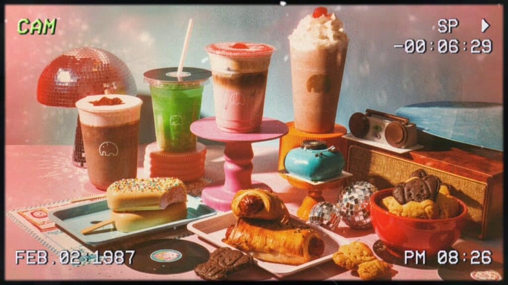 We Coffee Nostalgiacore: bebidas e doces em estética retrô Mesa com bebidas e doces do cardápio Nostalgiacore da We Coffee, em estilo retrô com câmera analógica.