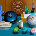 Conjunto de utensílios da Le Creuset inspirado em Star Trek sobre mesa azul, com formas e panelas temáticas.