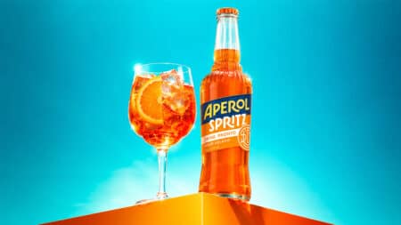Aperol Spritz pronto para beber em garrafa de 275 ml Garrafa de Aperol Spritz pronto para beber e taça com bebida alaranjada sobre fundo azul