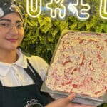 Funcionária da Borelli mostra bandeja de gelato de Morango Cravejado em cenário decorado com folhagens e luzes neon.