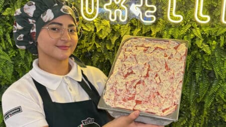 Funcionária da Borelli mostra bandeja de gelato de Morango Cravejado em cenário decorado com folhagens e luzes neon.