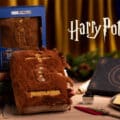 Embalagem e pelúcia interativa do Livro dos Monstros de Harry Potter em cenário de Natal da Cacau Show.