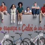 Família sentada com bicicletas ao fundo e texto “Não esqueça a Caloi do seu filho” em campanha da Caloi.