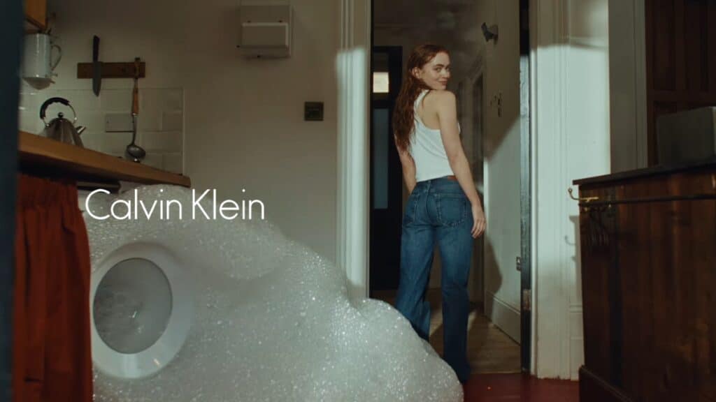 Sadie Sink na campanha Calvin Klein Sadie Sink em campanha da Calvin Klein, em cena interna com iluminação suave e marca Calvin Klein ao fundo.