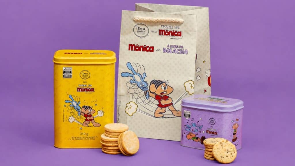 Latas colecionáveis Dona do Doce e Turma da Mônica Embalagens e latas colecionáveis da Dona do Doce com Turma da Mônica, sobre fundo roxo, com bolachas