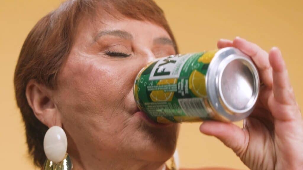 Pessoa com olhos fechados tomando refrigerante FYS, segurando uma lata verde e amarela na boca em campanha.