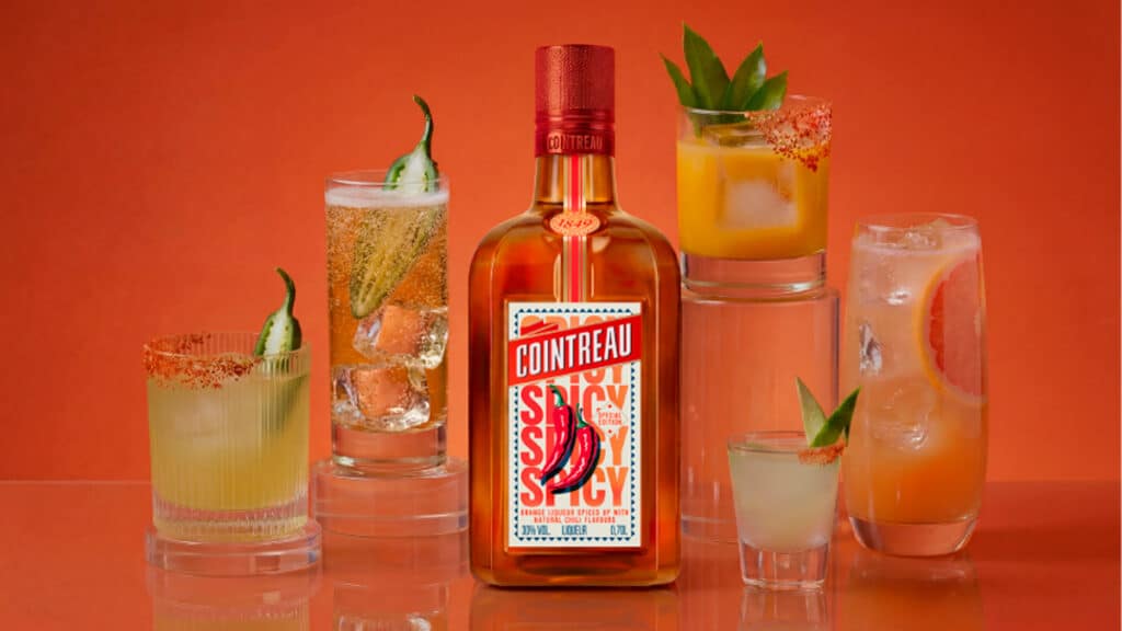 Cointreau Spicy e coquetéis com pimenta e pepino Garrafa do licor Cointreau Spicy com coquetéis ao lado, em fundo laranja, com pimenta e pepino como decoração