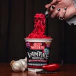 Cup Noodles Vampire Noodles de Halloween em uma mesa, com macarrão vermelho sendo servido e elementos do tema assustador.