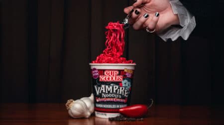 Cup Noodles Vampire Noodles Halloween com macarrão vermelho Cup Noodles Vampire Noodles de Halloween em uma mesa, com macarrão vermelho sendo servido e elementos do tema assustador.