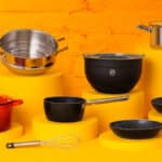Conjunto de utensílios MasterChef Brasil, com panelas e acessórios sobre fundo amarelo, promovendo campanha do ClubeFato