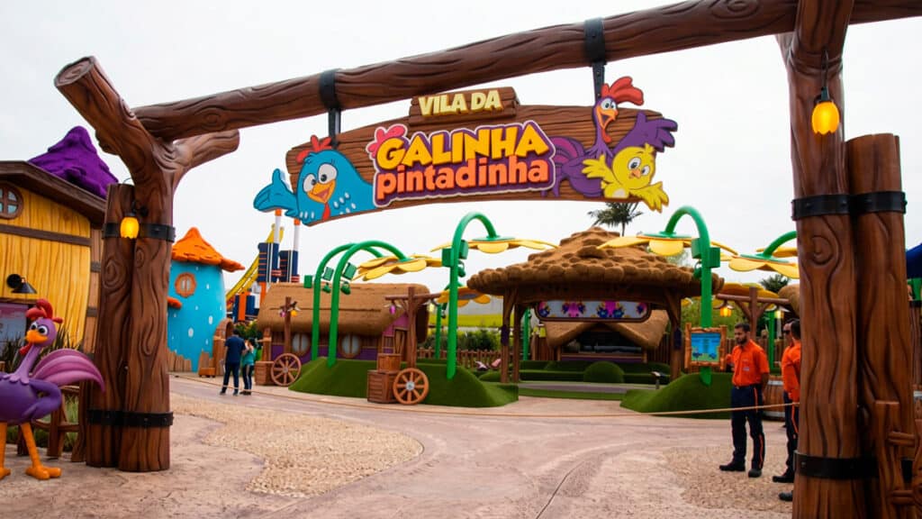 Entrada da Vila da Galinha Pintadinha no Beto Carrero World, com placa temática e personagens ao fundo
