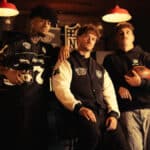 Homens usando jaquetas e acessórios em um bar, com garrafa ao fundo e referência à parceria Jack Daniel’s e NFL.