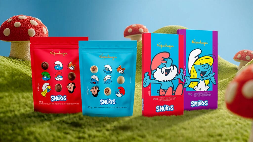 Embalagens de chocolate Kopenhagen com tema Smurfs, com personagens dos Smurfs, sobre grama e cogumelos coloridos ao fundo.