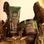 Produtos Bath & Body Works da linha Mandaloriano e Grogu em frascos e pote sobre troncos, com fundo claro.