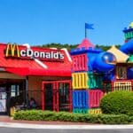Entrada do McDonald’s com parquinhos infláveis coloridos e brinquedos para crianças em frente ao restaurante.