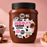 Pote do MooCream Proteico Milky Moo (creme de avelã com cacau e whey protein) com avela e colher ao lado.