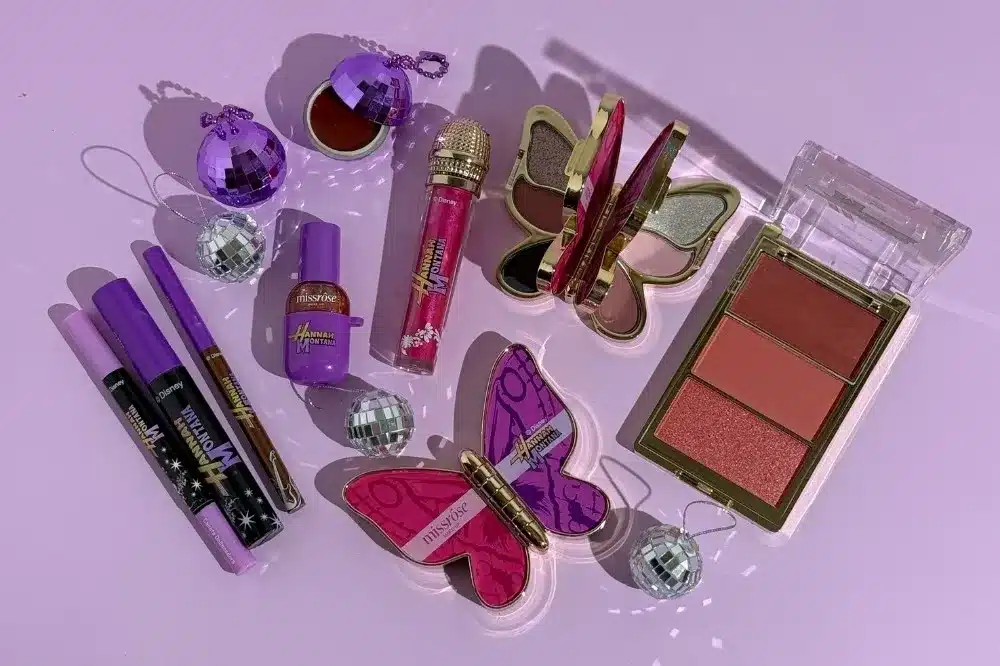 Linha de maquiagem da parceria Miss Rôse x Hannah Montana com batom, gloss, paleta e acessórios em tons roxos e rosas.