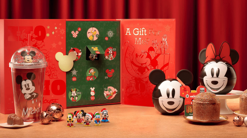Natal com Mickey e amigos: enfeites, presentes e doces Decoração de Natal com Mickey e amigos, enfeites e caixas temáticas em fundo vermelho, sobre mesa com doces e glass pot.