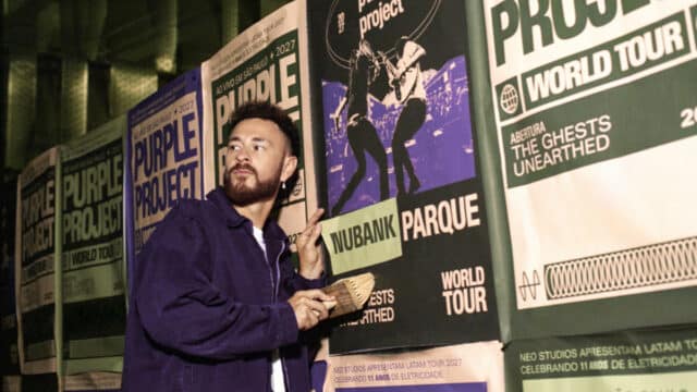 Homem em palco segurando papel ao lado de banners com a marca Nubank Parque, durante evento do Purple Project World Tour.