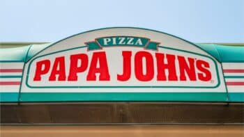 Papa Johns Brasil: letreiro na fachada Fachada da loja com o letreiro “PAPA JOHNS” e o nome PIZZA em destaque.