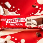 Embalagem da barra proteica Prestígio Nutrata Nestlé, 11g de proteína, com chocolate e coco ralado, sobre fundo vermelho