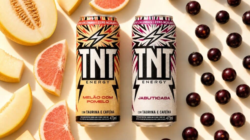 Latas de TNT Energy Drink sabores Melão com Pomelo e Jabuticaba com porções de frutas ao fundo.
