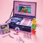 Kit de maquiagem da Martine Cosmetics com paleta e acessórios temáticos de Três Espiãs Demais em cores roxas e rosa.