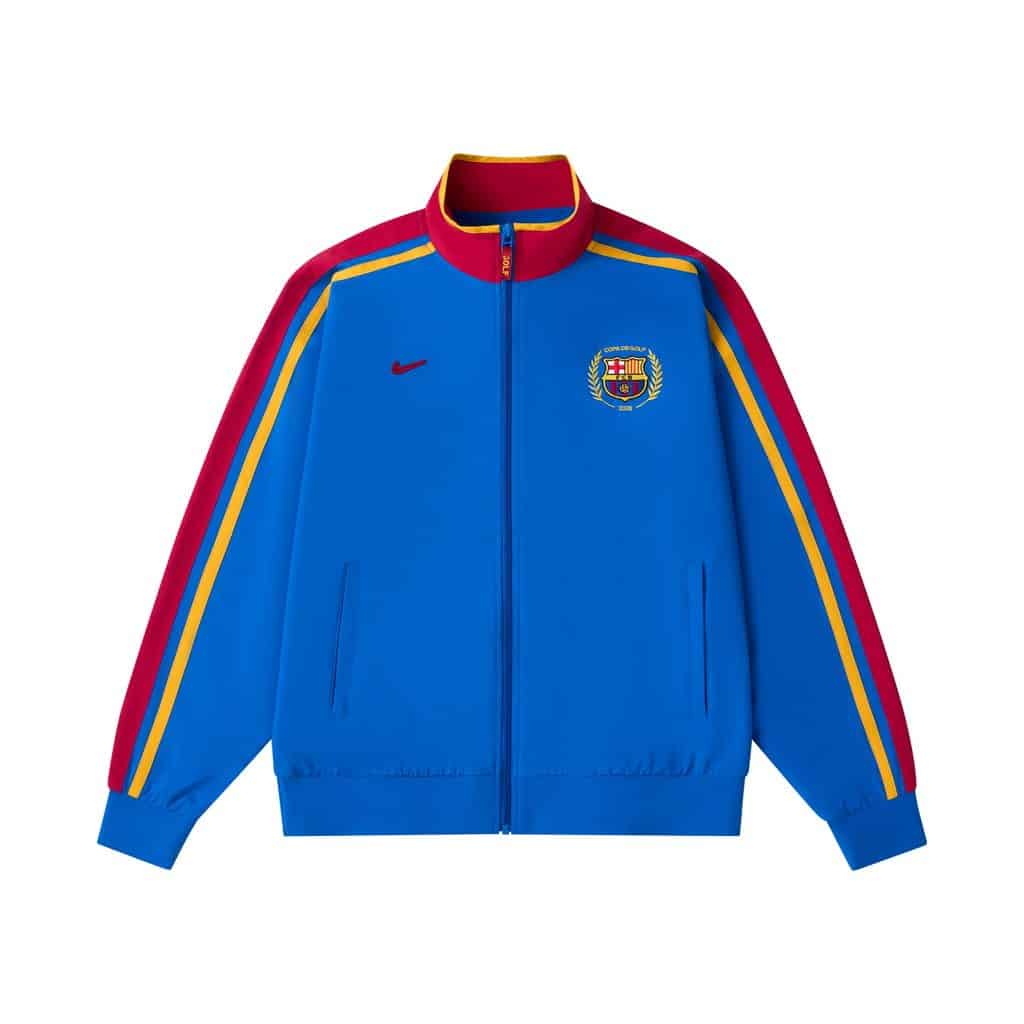 Jaqueta esportiva azul do Barcelona com detalhes vermelhos, dourados e emblema do clube no peito.