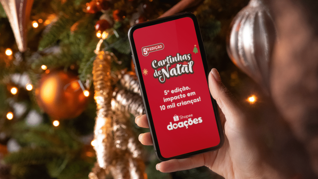 Celular com anúncio da 5ª edição “Cartinhas de Natal” da Shopee Doações durante clima de Natal.
