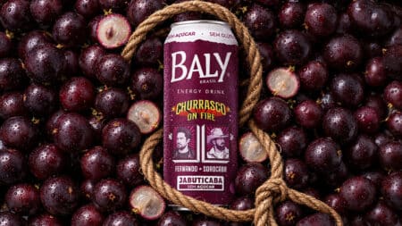 Baly Jabuticaba energético com rótulo e jabuticabas Garrafa de energético Baly Jabuticaba com corda, ao lado de jabuticabas em fundo escuro.